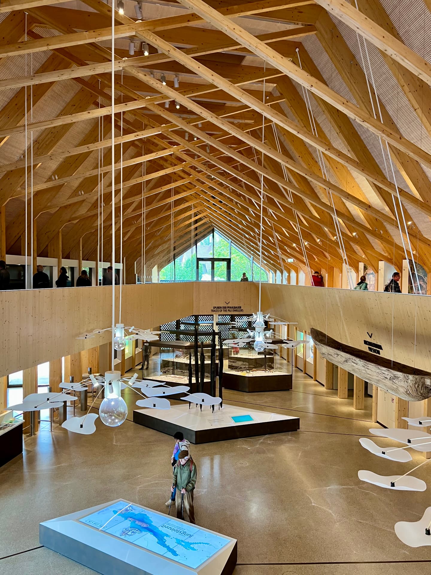 Innenraum eines Holzbaus mit sichtbarer Dachkonstruktion und Ausstellung