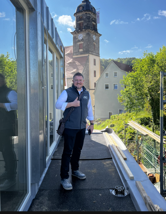 Richard Gunkel auf einer Baustelle mit historischem Kirchturm im Hintergrund
