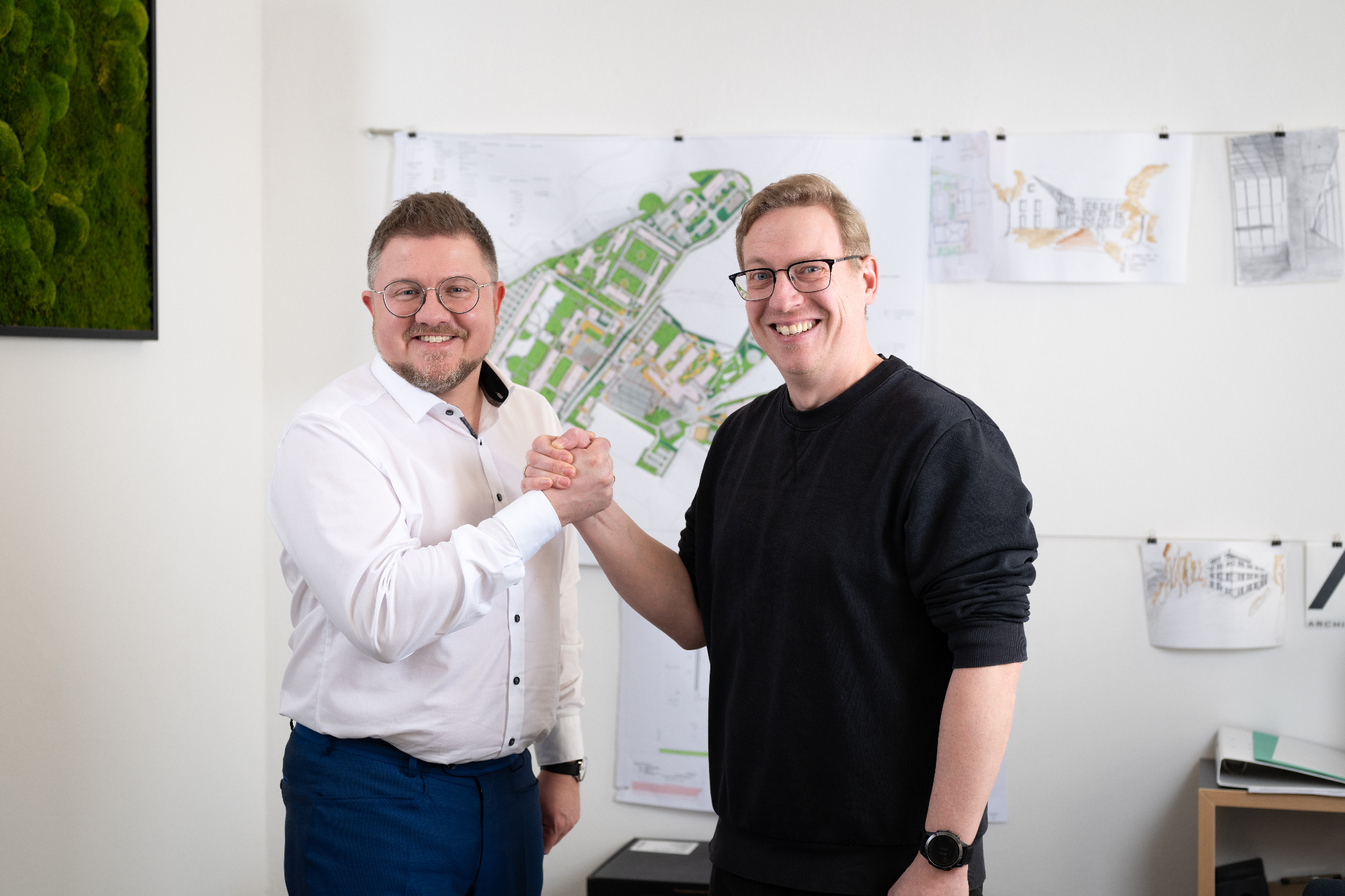 Zwei ARC1-Kollegen beim Handschlag vor Projektplänen